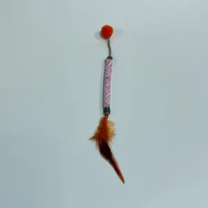 Macro detail of natural cat silvervine stick toy with soft feathers and an orange pompom.