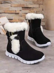 Detailed view of women's black snow boots with white faux fur trim and pom-poms.