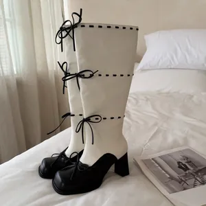 Primo piano di stivali alti neri e bianchi con fiocchi decorativi su letto bianco