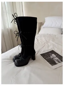 Eleganti stivali neri alti al ginocchio con fiocchi e tacco largo posati sul letto.