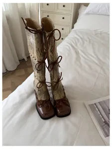 Dettaglio di eleganti stivali alti con fiocchi appoggiati su un accogliente letto bianco.