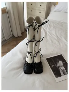 Vista dettagliata di stivali alti panna e neri con fiocchi decorativi sul letto