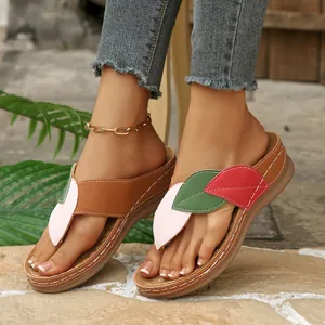 Primer plano de chanclas de cuña para mujer con parches de hojas de colores sobre piedra