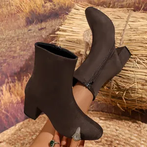 Detailed close-up of dark brown suede ankle boots featuring side zipper and chunky heel