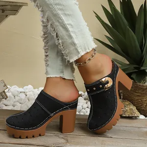 Detail view of black hollowed-out clogs with chunky high heels and platform soles.