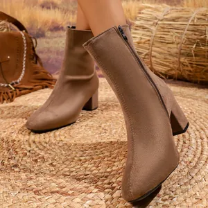 Close-up of brown suede ankle boots with block heel shown on model in rustic setting