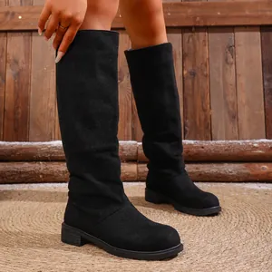 Detailed view of women's black slouchy knee-high boots on rustic wooden background.