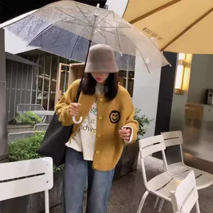 Mustard yellow knit cardigan featuring an embroidered smiley face in an outdoor street setting