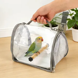 A hand holding the handle of a clear bird carrier with a parrot resting inside