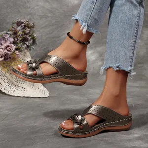Detaillierte Seitenansicht von metallgrauen Keilsandalen mit Retro-Blumendekor auf einem Modell.
