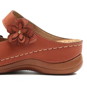 Detailaufnahme der braunen Retro-Keilsandale mit Blumenverzierung und weißen Nähten
