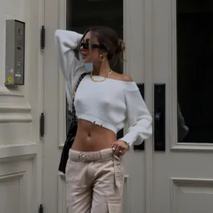 Sexy off-the-shoulder white cropped knitted sweater with distressed hem detailing on model