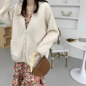 Detailed view of a cream white loose knit cardigan featuring a V-neck and front pockets