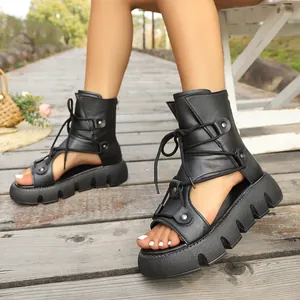 Detailansicht schwarzer Plateau-Sandalen mit Schnürung im Gladiator-Stil auf Holz.