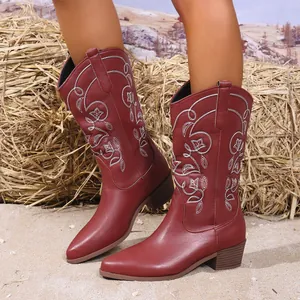 Detail van rode cowboylaarzen met wit borduursel in rustieke buitenomgeving.