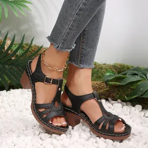 Detailed view of black peep toe block heel sandals worn on white pebbles.