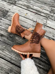 Nahaufnahme brauner Schnürstiefel mit Metallnieten auf rustikalem Holzsteg im Freien