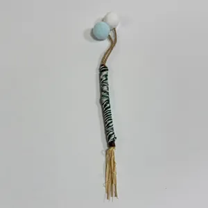 Detailed view of a natural cat chew stick with soft blue pom-poms and a straw tassel