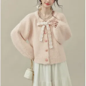 Dettaglio dell'elegante cardigan rosa in maglia con fiocco di fiori e bottoni a cuore.