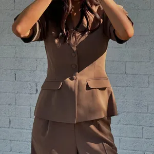 Détail d'un ensemble blazer à manches courtes et pantalon marron sur un mur blanc.