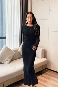 Elegant woman in a sexy long-sleeved black mesh maxi beach cover-up dress in a cozy room.
