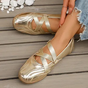 Detail of gold metallic Mary Jane flats with cross straps and soft sole on wooden floor.