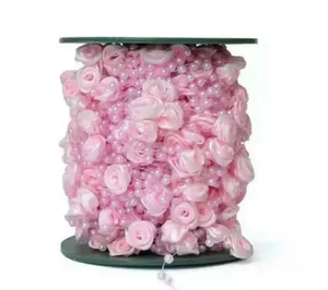 Close-up of pink fabric rose and pearl bead trim on a spool for DIY bridal accessories