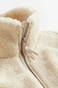 Nahaufnahme einer cremefarbenen Sherpa-Fleecejacke mit Metallreißverschluss