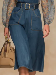 Detail view of high-waisted denim jumpsuit featuring large pockets and belt buckle.