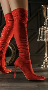 Nahaufnahme von glamourösen roten Overknee-Stiefeln mit Strasssteinen und Pfennigabsatz.