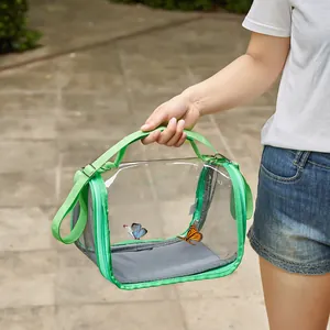 Close-up of portable transparent bird carrier bag with green trim in outdoor setting.