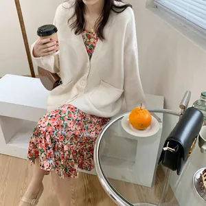 Beige knit cardigan detail featuring front pockets and button closure in a cafe setting.