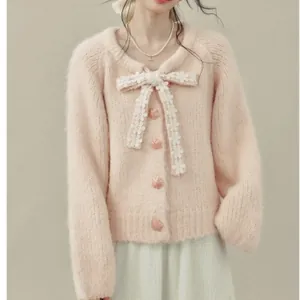 Dettaglio di cardigan in maglia rosa con grande fiocco di pizzo bianco e bottoni a fiore