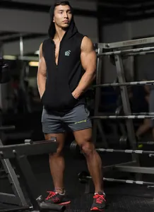 Professional athletic male model wearing a black sleeveless hooded gym vest and grey shorts
