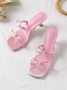 Nahaufnahme von rosa Sandaletten mit Pfennigabsatz und eleganten Schleifen auf weißem Stoff