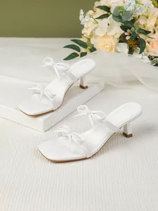 Elegante Nahaufnahme weißer Kitten-Heel-Sandalen mit quadratischer Zehenpartie und Schleifen