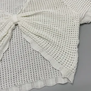 Dettaglio del crop top bianco in maglia traforata con fiocco frontale e bordo pizzo