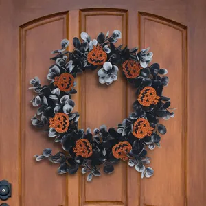 Halloween black leaf wreath with glittery orange pumpkins hanging on a rustic wooden door