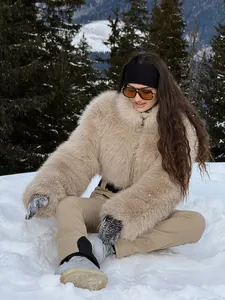 Close-up of stylish beige faux fur ski suit outfit in a snowy mountain landscape