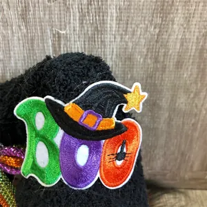 Detailed close-up of colorful embroidered BOO letter patch with witch hat on Halloween gnome doll
