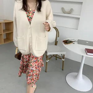 Detailed view of cream loose knit cardigan with V-neck and pockets over floral dress