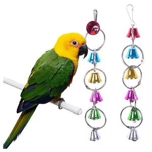 Set of colorful metal hanging bell toys for parrots shown next to a bird on a perch