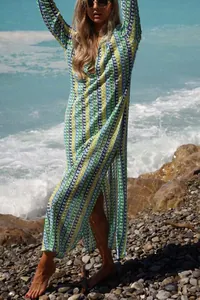 Elegante donna con vestito lungo in maglia a righe e scollo a V su una spiaggia rocciosa