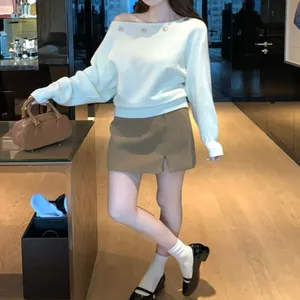 Detalle de jersey blanco con hombros descubiertos y adorno de botón en un look chic