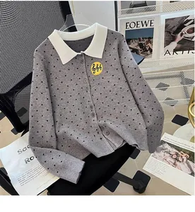 Detailed view of a grey polka dot knitted cardigan with a white lapel and musical badge.