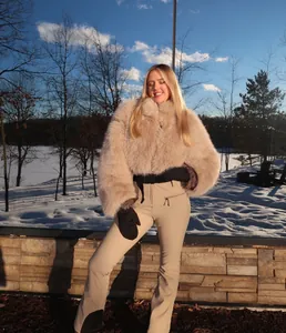 Woman wearing beige faux fur coat and slim fit ski pants in outdoor snowy setting