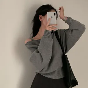 Dettaglio di un maglione grigio a trecce con scollo diagonale e spalle scoperte.