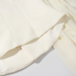 Close-up of cream blazer hem showing precise stitching and smooth fabric texture.