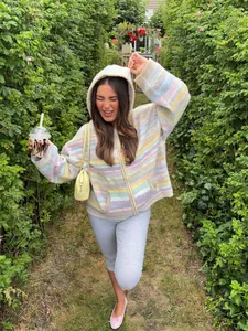 Lifestyle view of a woman wearing a colorful striped hooded knit cardigan in a green garden
