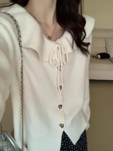 Close-up detail of cream knit doll-collar cardigan with heart buttons and bow tie